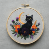 close-up-black-cat-sitting-flowered-surface